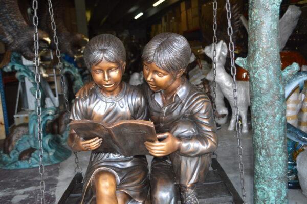 Kids on Swing Set Reading a Book Life Size Bronze Statue -  50"L x 40"W x 70"H.