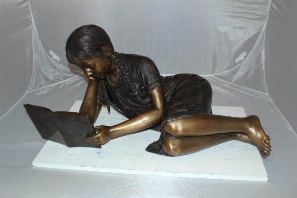 Girl laying reading a book Bronze Statue -  Size: 36"L x 17"W x 18"H.