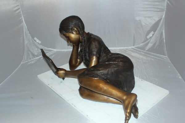 Girl laying reading a book Bronze Statue -  Size: 36"L x 17"W x 18"H.