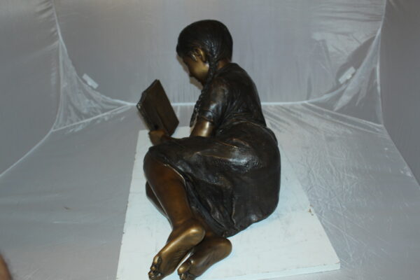 Girl laying reading a book Bronze Statue -  Size: 36"L x 17"W x 18"H.