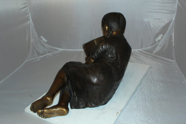 Girl laying reading a book Bronze Statue -  Size: 36"L x 17"W x 18"H.
