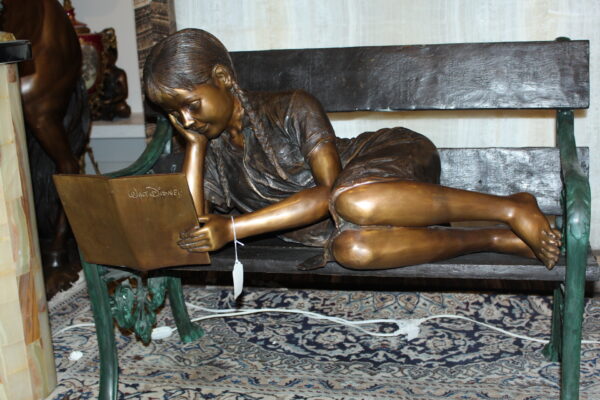 Girl laying on a bench reading a book Bronze Statue -  Size: 27"L x 39"W x 32"H