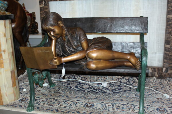 Girl laying on a bench reading a book Bronze Statue -  Size: 27"L x 39"W x 32"H