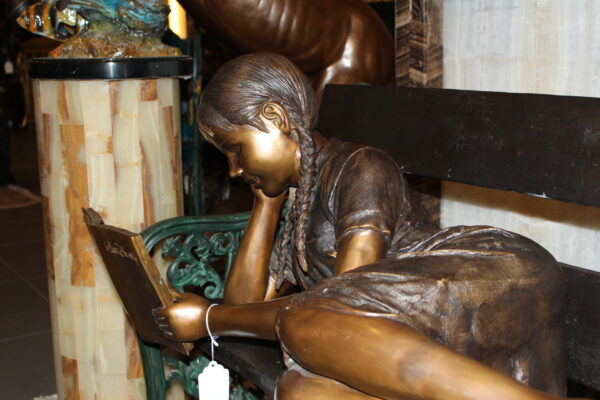 Girl laying on a bench reading a book Bronze Statue -  Size: 27"L x 39"W x 32"H