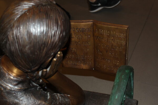 Girl laying on a bench reading a book Bronze Statue -  Size: 27"L x 39"W x 32"H