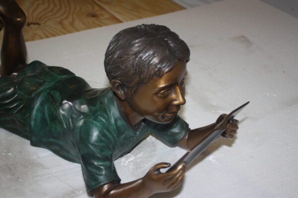 boy laying reading book bronze Statue -  Size: 24"L x 10"W x 11"H.