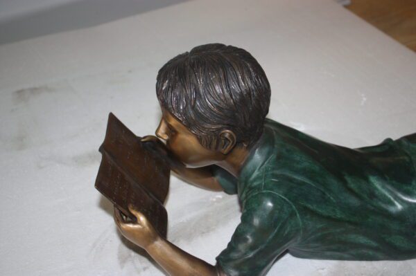 boy laying reading book bronze Statue -  Size: 24"L x 10"W x 11"H.