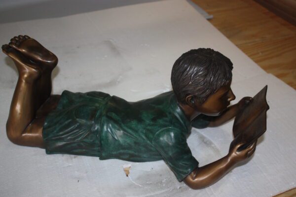 boy laying reading book bronze Statue -  Size: 24"L x 10"W x 11"H.